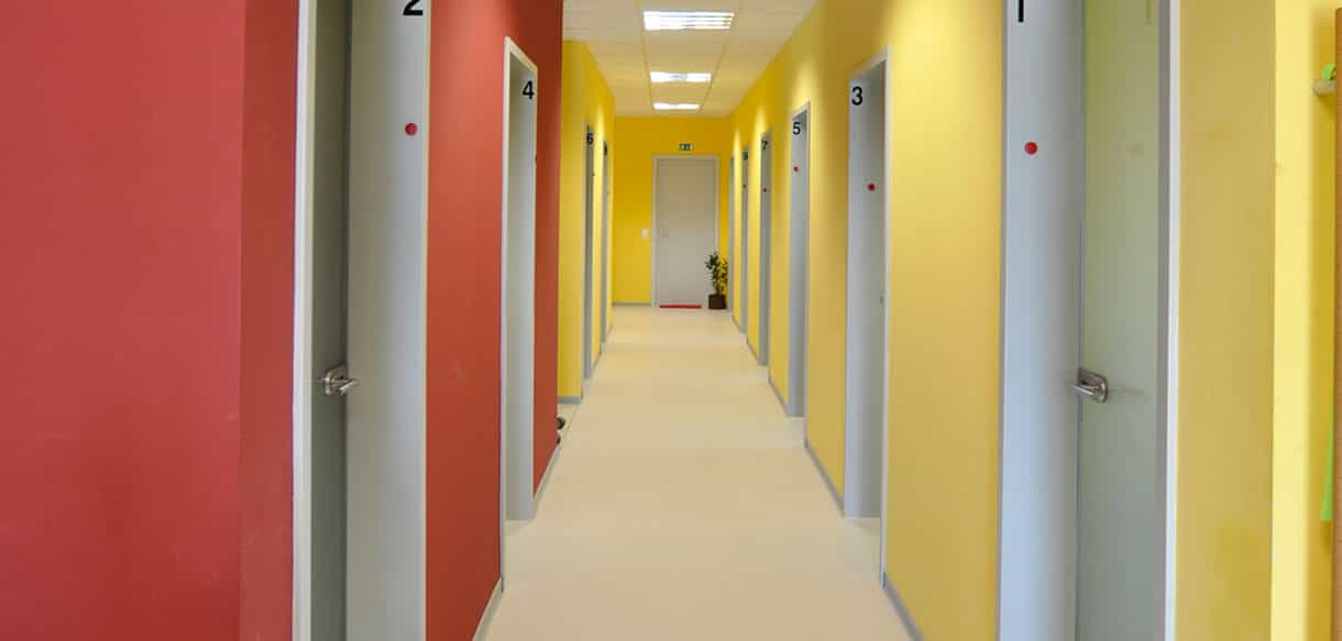 Flur der Arcus Physiotherapiepraxis mit nummerierten Behandlungsräumen und rot-gelben Wänden