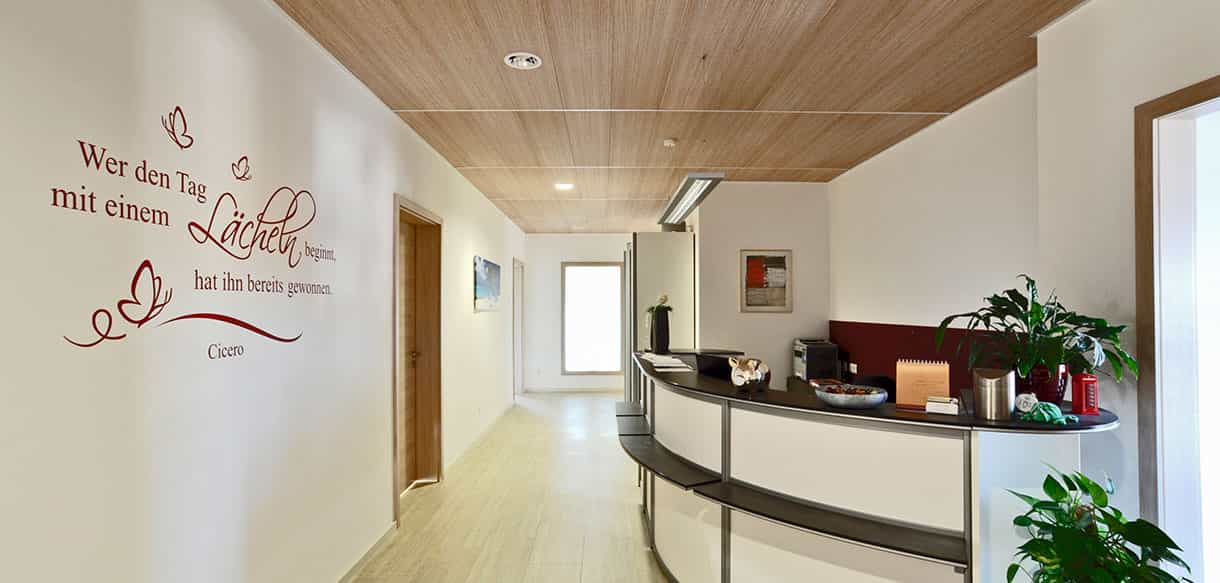 Flur mit Empfangstheke, Holzdecke und Wandtattoo in der Physiotherapiepraxis Zielke