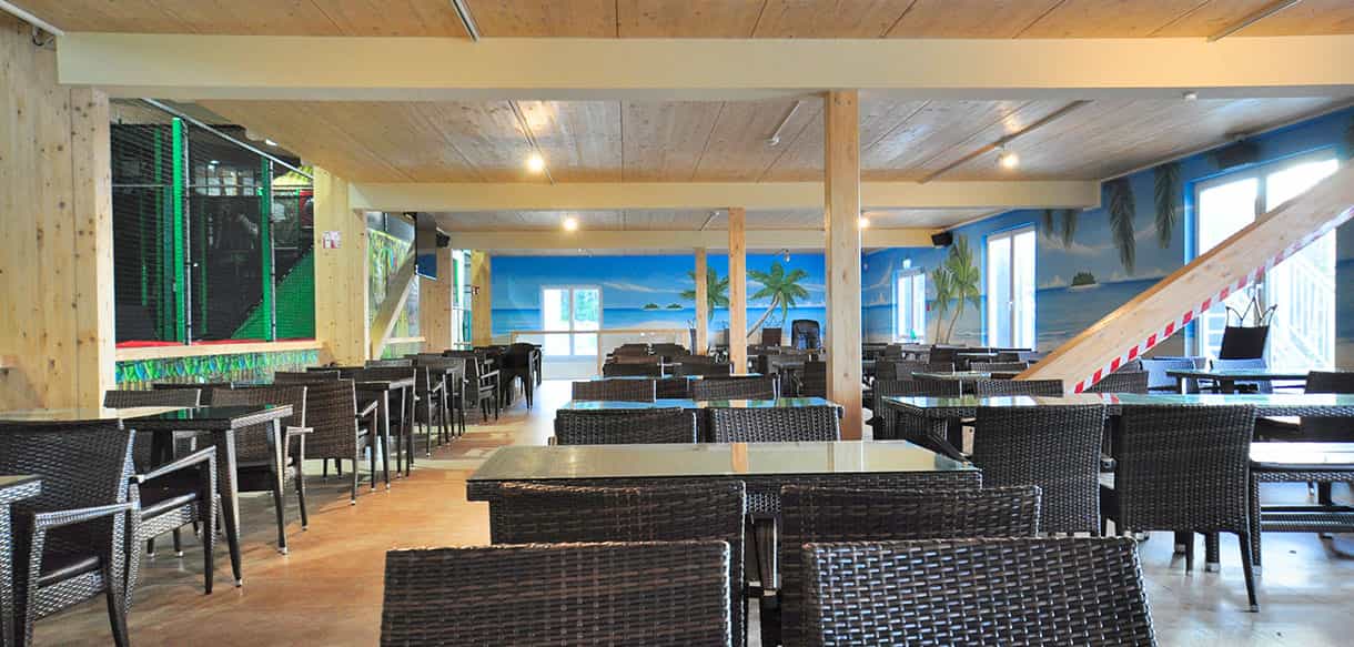Gastronomiebereich des Kibungu Indoor-Spielparadieses mit Tischen, Holzdecke und Wandmalerei
