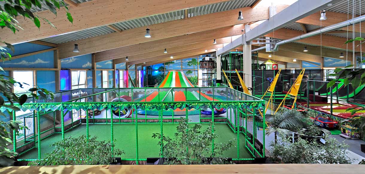 Blick über die Spielhalle von Kibungu mit Klettergerüst und bunten Rutschen unter Holzbindern