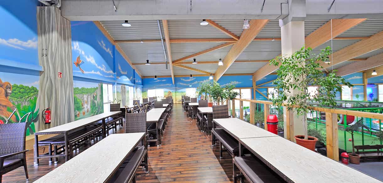Sitzbereich mit langen Tischen und Dschungel-Wandmalerei im Kibungu Indoor-Spielparadies