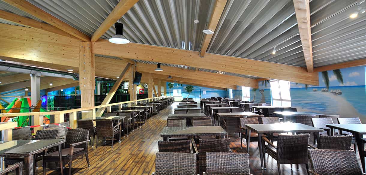 Gastrobereich mit Rattanstühlen unter dem Holzdach des Kibungu Indoor-Spielparadieses