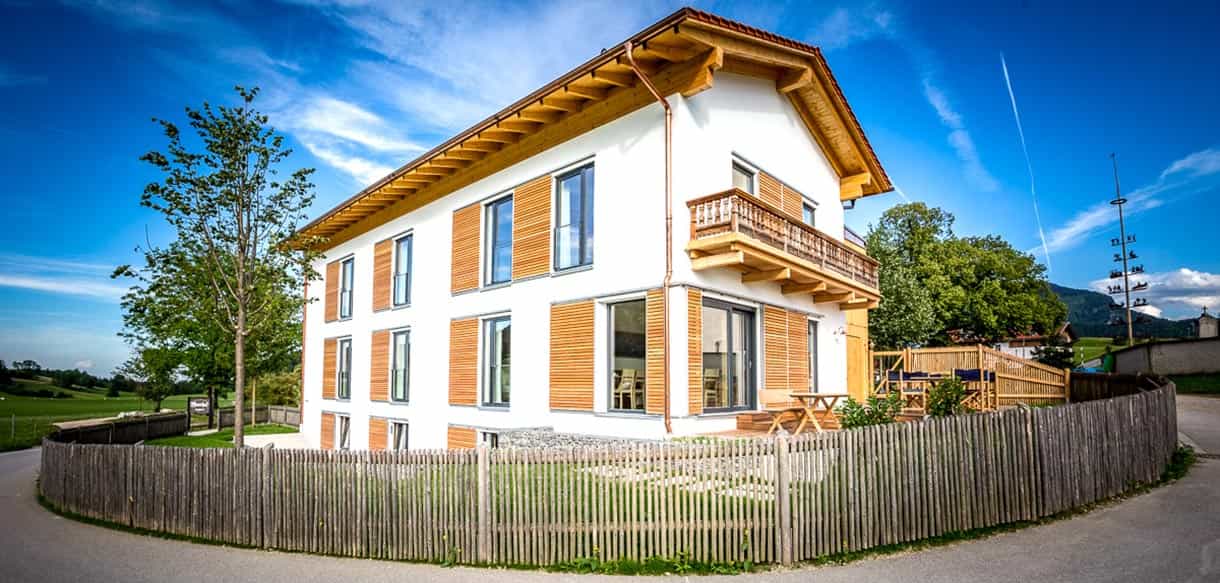 Gästehaus des Moarhof Roßholzen am Samerberg mit Holzbalkonen, weißer Fassade und Holzzaun