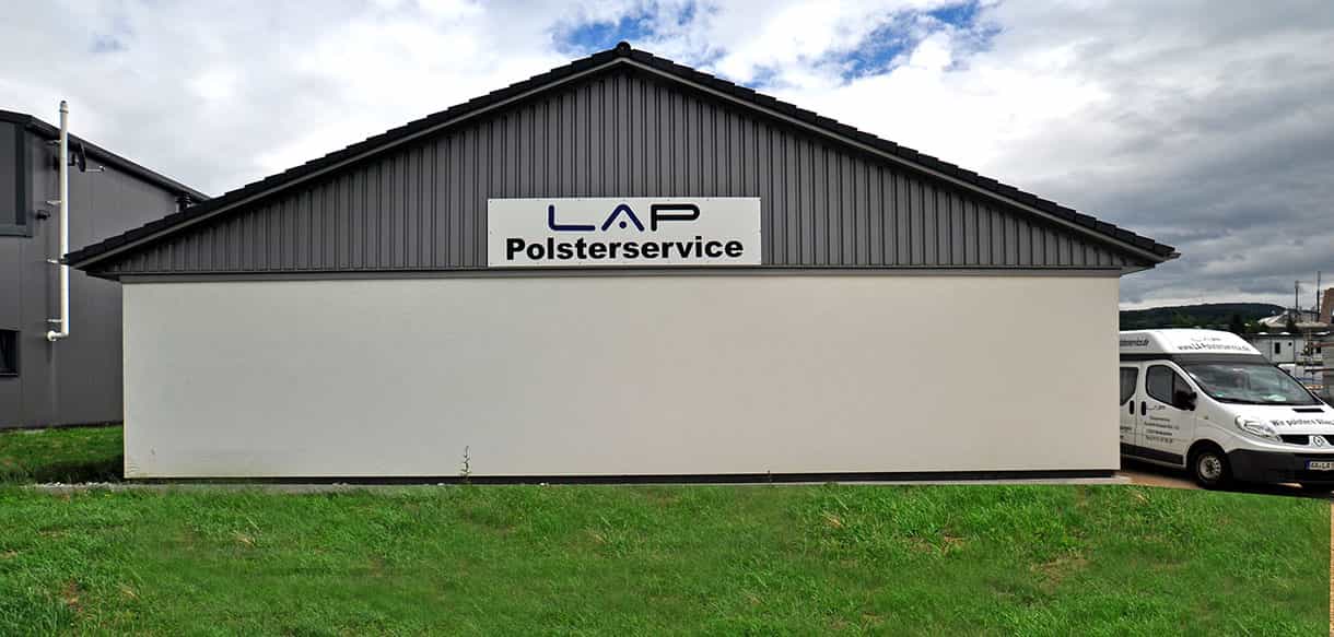 Giebelseite des Betriebsgebäudes LA Polsterservice mit Firmenschild und Wiese