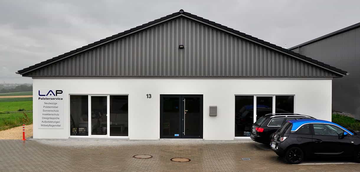 Eingangsseite des Betriebsgebäudes LA Polsterservice mit Schaufensterverglasung und Parkplatz