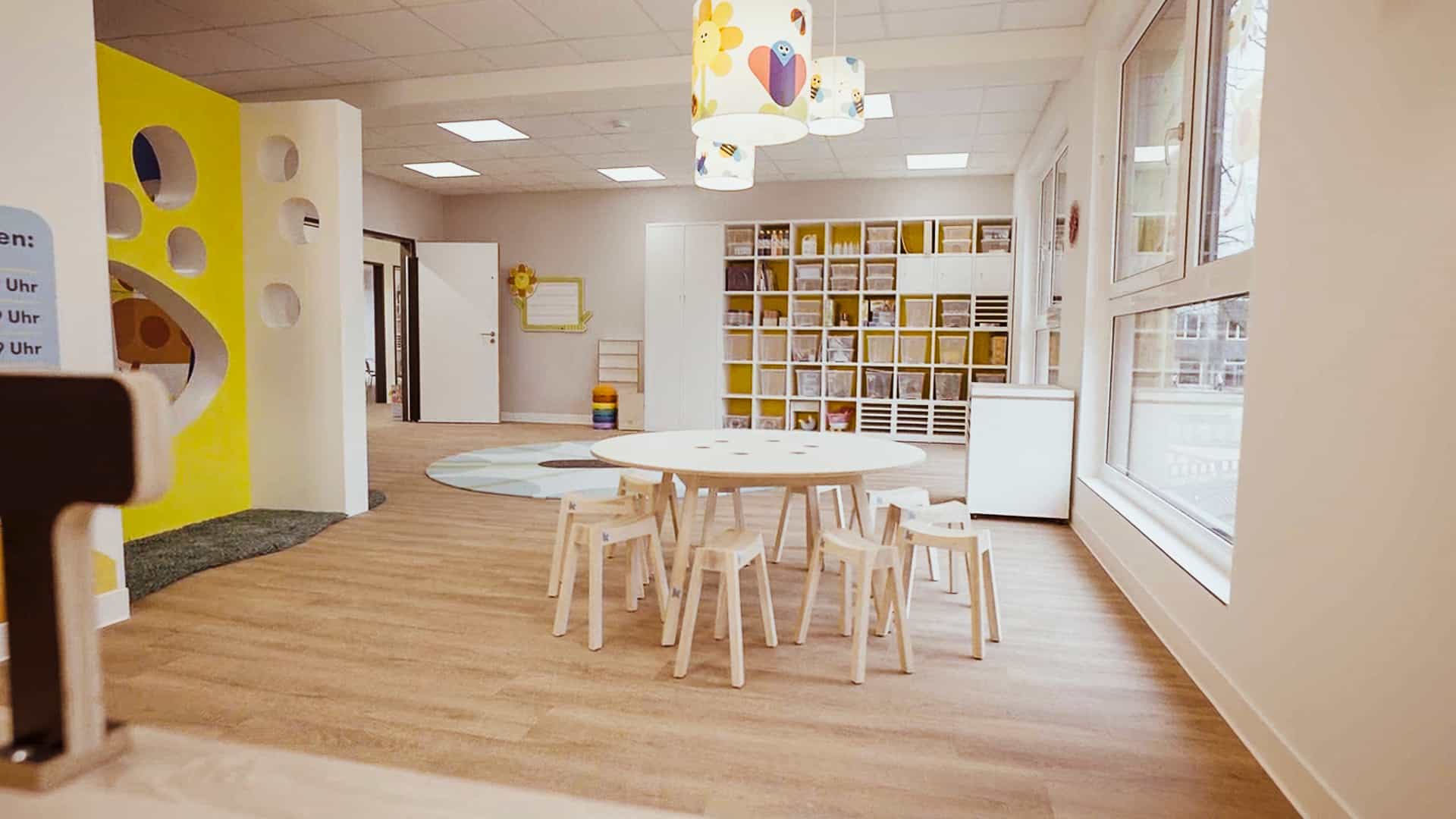 Gruppenraum mit rundem Kindertisch, Hockern und Fächerregal in der Kita Hamburg