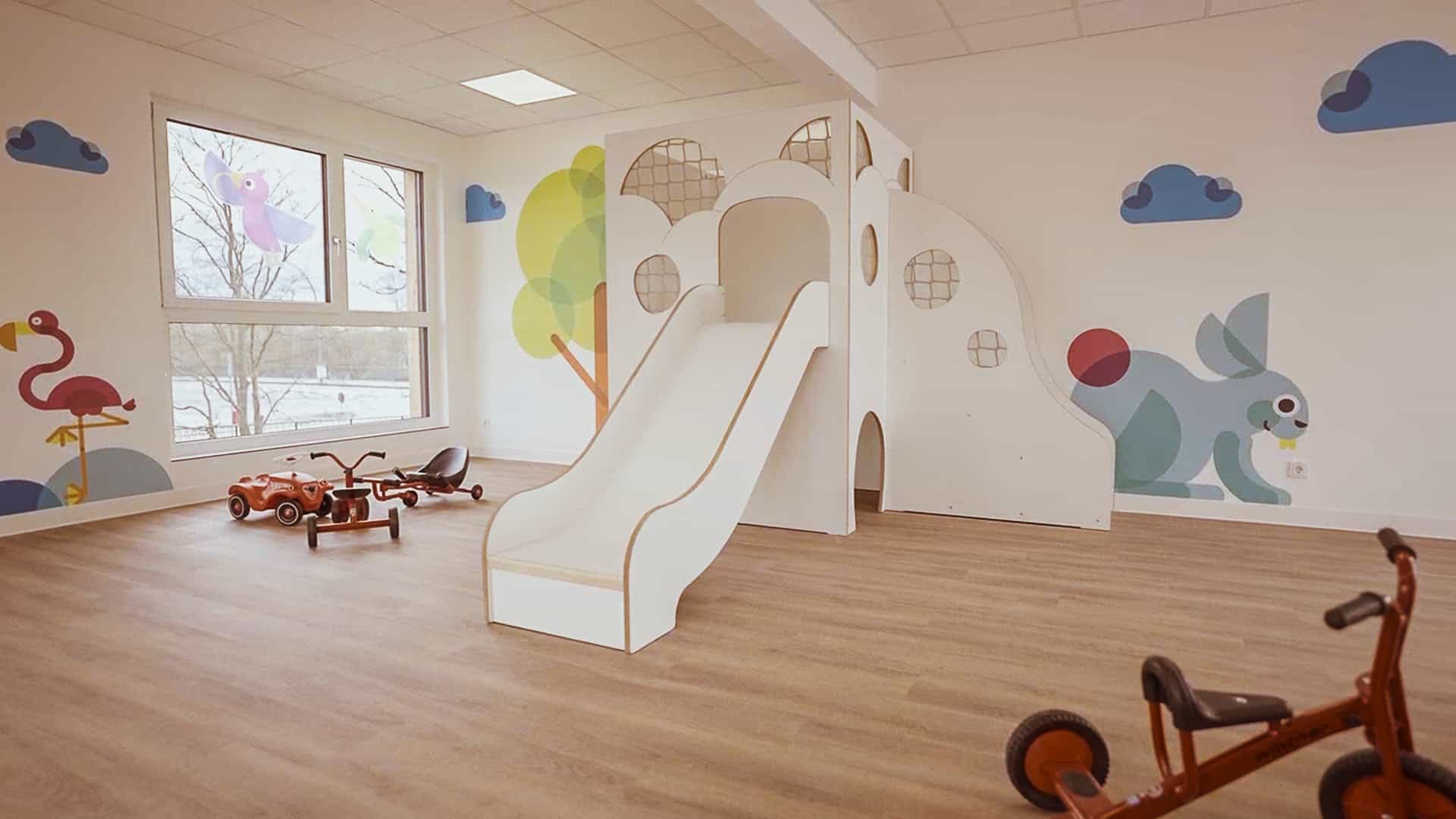 Weiße Rutsche mit Treppe und Dreiräder im Bewegungsraum der Kita von Klüver & Kompanie