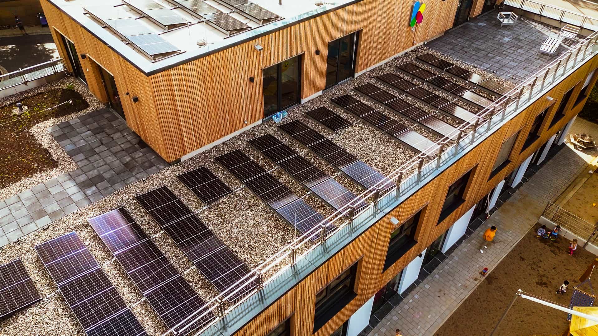 Luftaufnahme des Flachdachs der Kita Hamburg mit Photovoltaikmodulen und Holzfassade