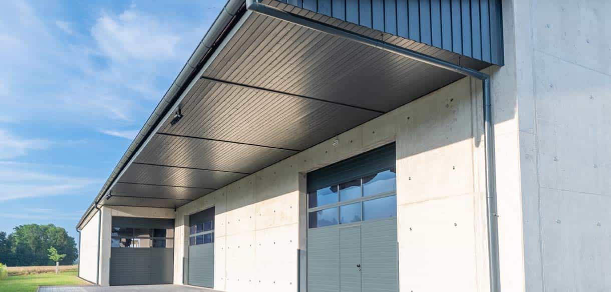 Nagelplattenbinderhalle in Fahrenzhausen mit grauer Fassade, Betonsockel und Sektionaltor