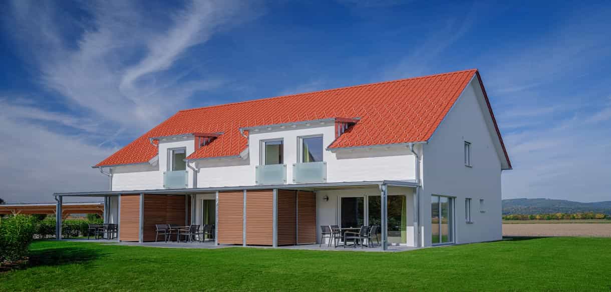 Ferienhaus mit rotem Ziegeldach, Holzelementen und Terrasse im Bachhof Resort Kirchroth von Haas Fertigbau