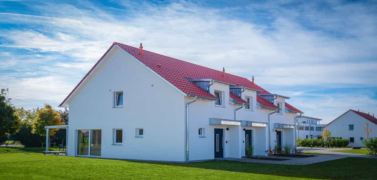 Drei Ferienhäuser mit roten Ziegeldächern und weißer Fassade im Bachhof Resort Kirchroth von Haas Fertigbau