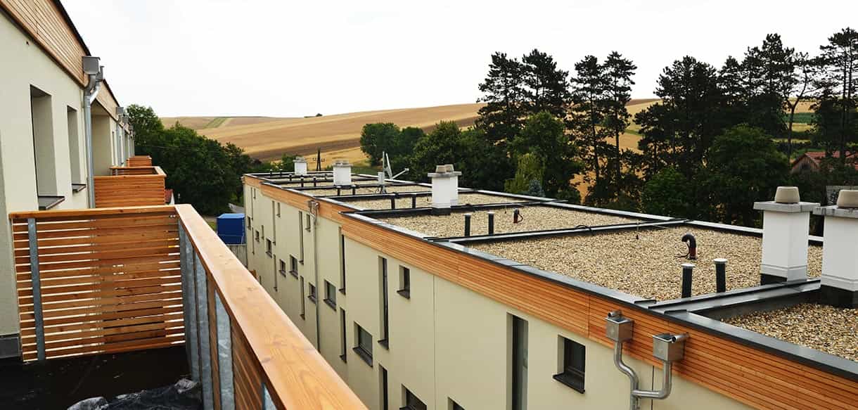 Blick über Holzsichtschutz und Flachdächer der Reihenhäuser in Mistelbach in die Landschaft