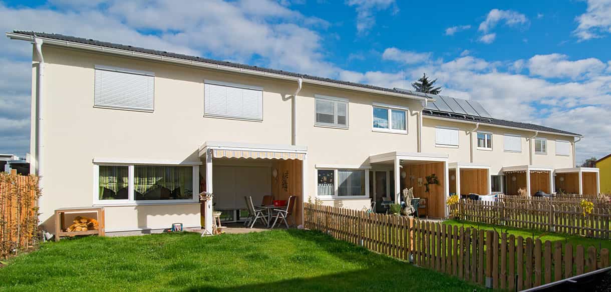 Gartenseite der fünf Reihenwohnungen mit Terrassen und Lattenzaun, Wohnungsbauanlage von Haas Wohnbau