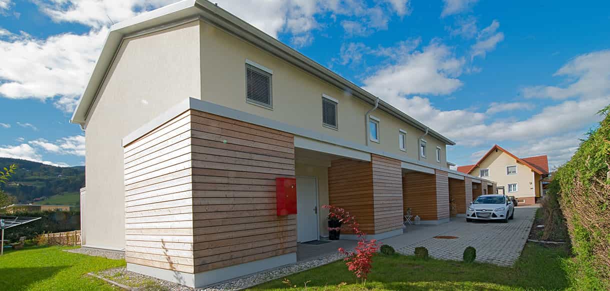 Giebelseite der Reihenwohnanlage mit holzverkleideten Carports und Eingangsbereich von Haas Wohnbau