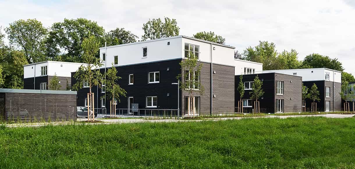 Blick über die Wiese auf mehrere Wohnhäuser des Donau-Wohnparks mit Holzfassade und Staffelgeschoss