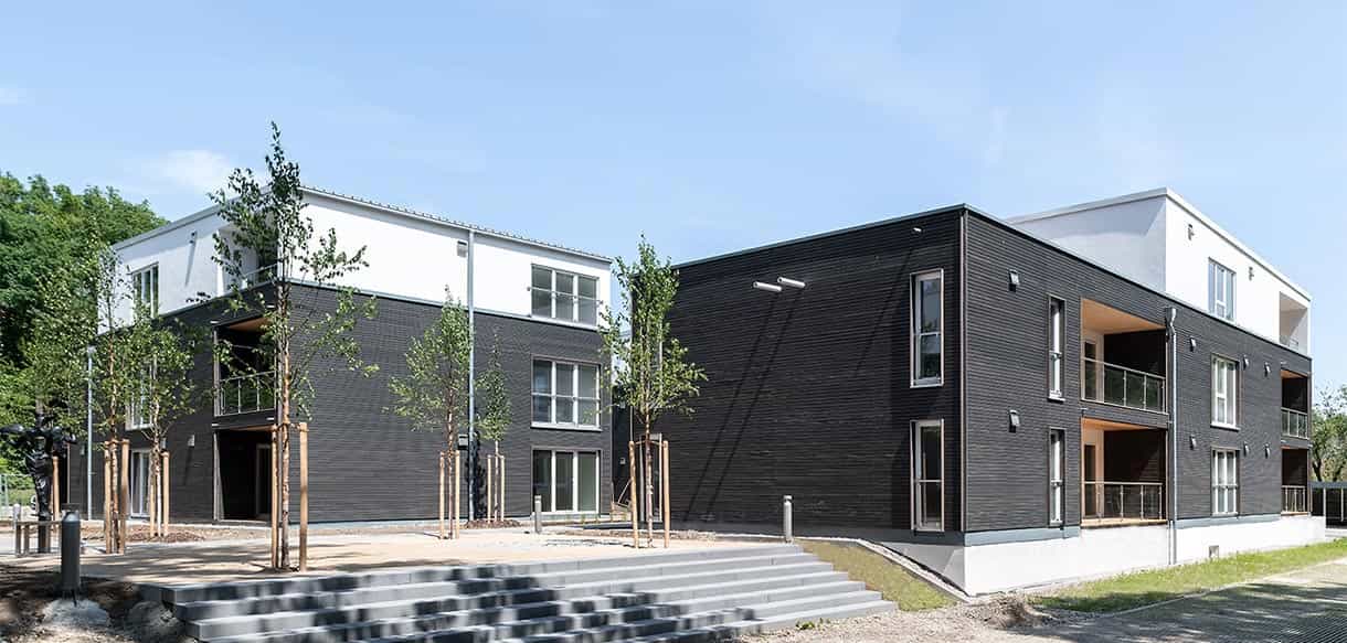 Zwei Wohnhäuser des Donau-Wohnparks mit schwarzer Holzfassade und Eingangstreppe, 34 Wohneinheiten
