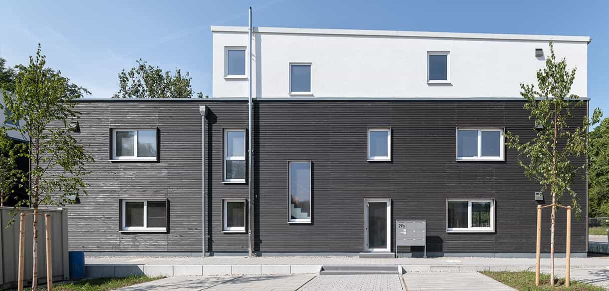 Frontansicht eines dreigeschossigen Wohnhauses mit Holzfassade und weißem Staffelgeschoss im Donau-Wohnpark