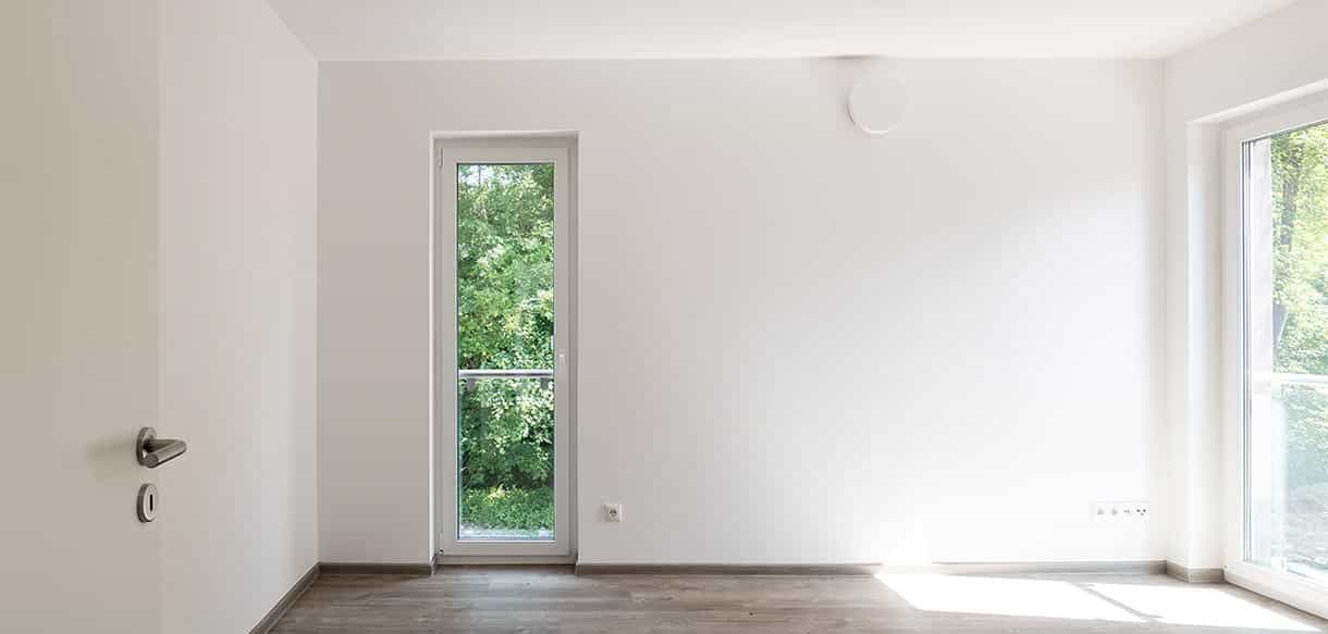 Leerer Wohnraum mit hohem Fenster und Parkettboden in einer Wohnung des Donau-Wohnparks