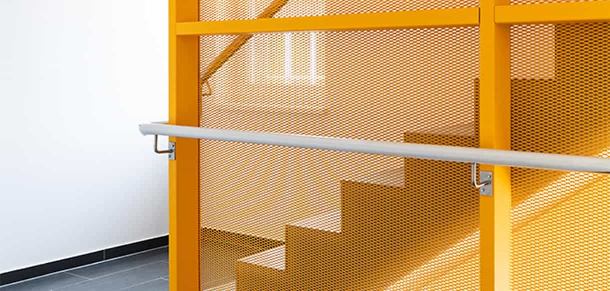 Treppenhaus mit orangefarbenem Lochblechgeländer und Handlauf in einem Wohnhaus im Donau-Wohnpark