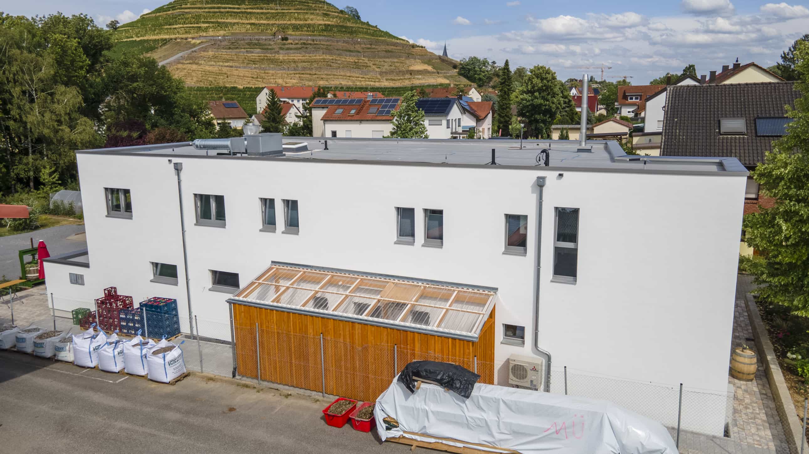 Luftaufnahme des Gastronomiegebäudes der Weinwirtschaft Burgblick mit Flachdach vor Weinbergen, Haas Gewerbebau