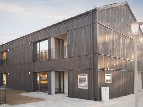 Mehrfamilienhaus von Haas Wohnbau mit vergrauter Holzfassade und Balkonen, Teaser zum Wohnbau-Katalog