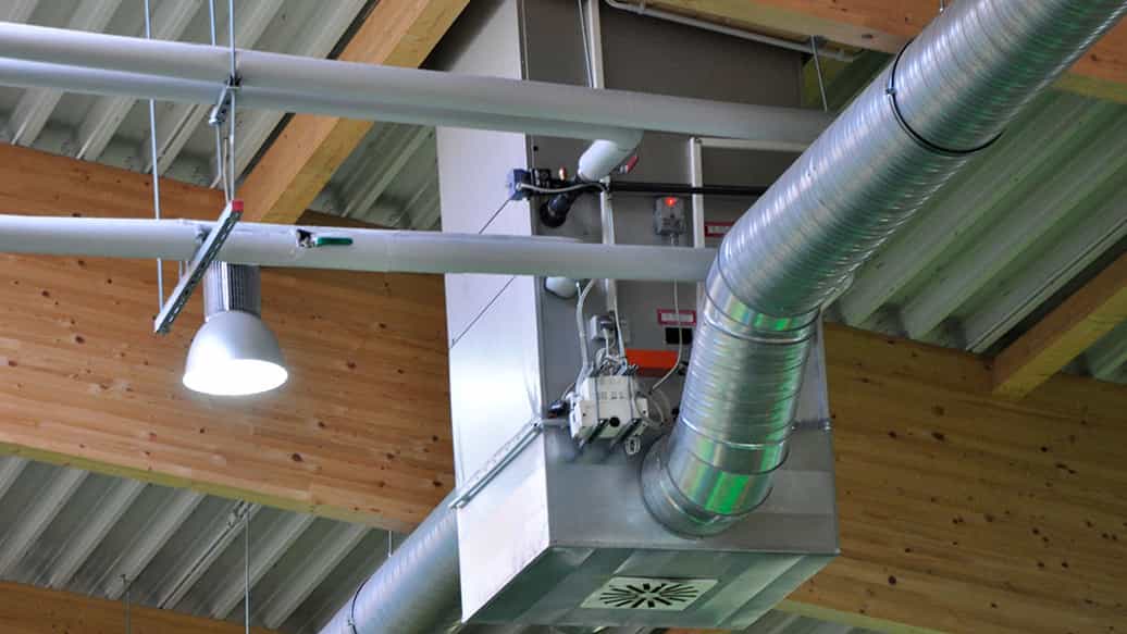 Detail der Holzdachkonstruktion mit Lüftungsrohren und Leuchte in der Spielhalle Kibungu