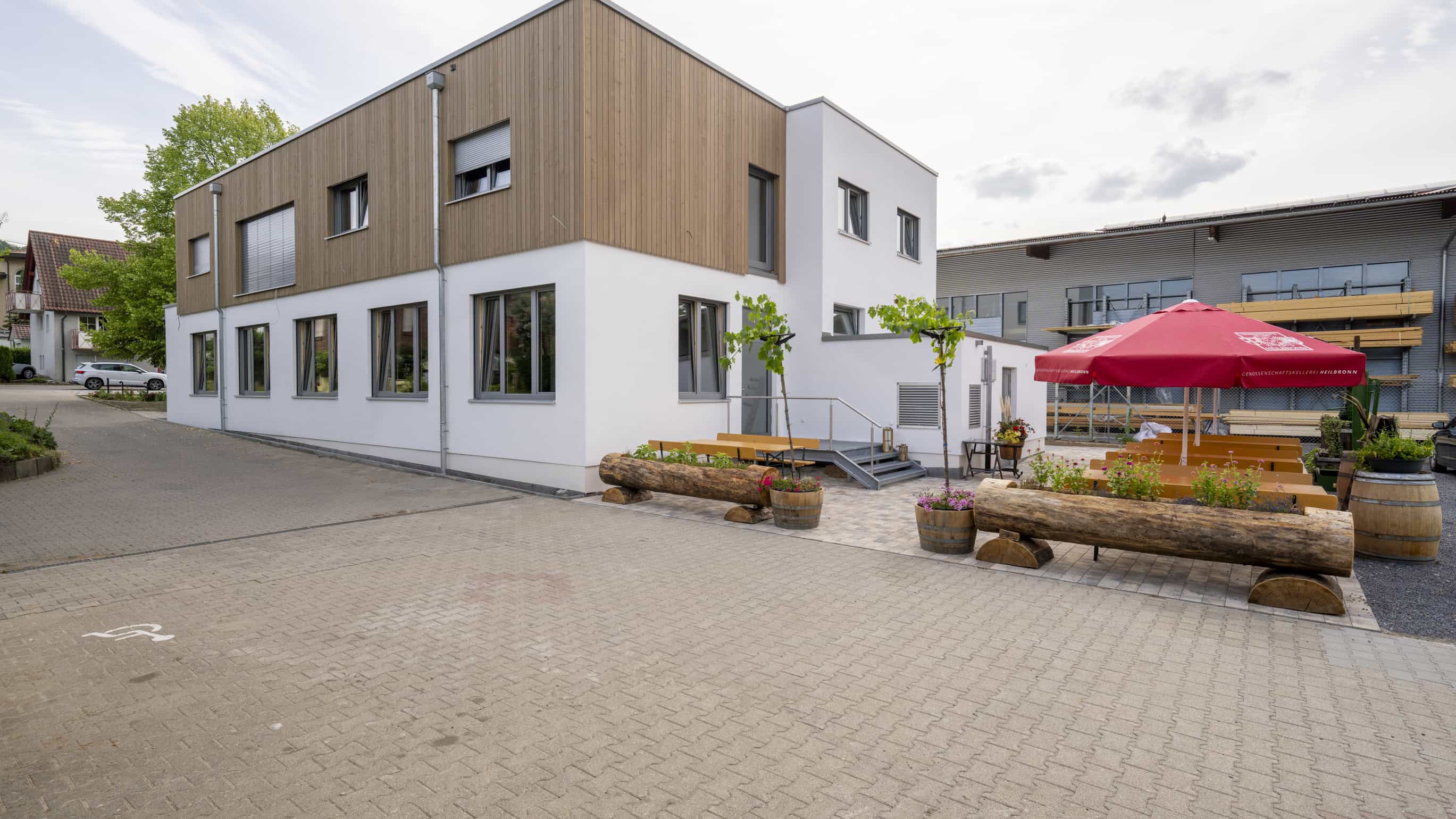 Gastronomiegebäude der Weinwirtschaft Burgblick mit Holzfassade im Obergeschoss und Außenterrasse mit Sonnenschirm