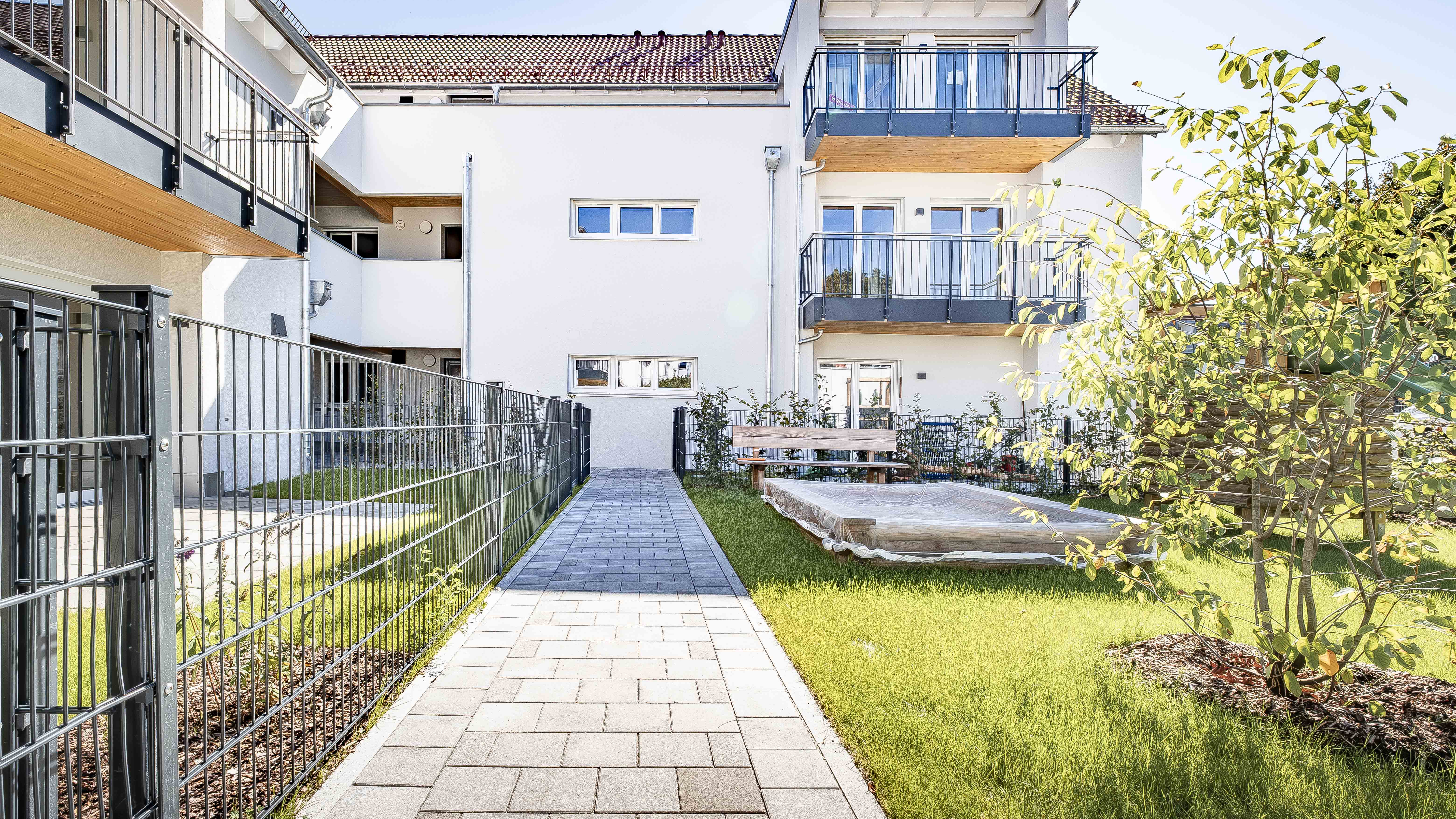 Gartenseite mit gepflastertem Weg und Balkonen der Wohnanlage mit 15 Wohneinheiten in Eching