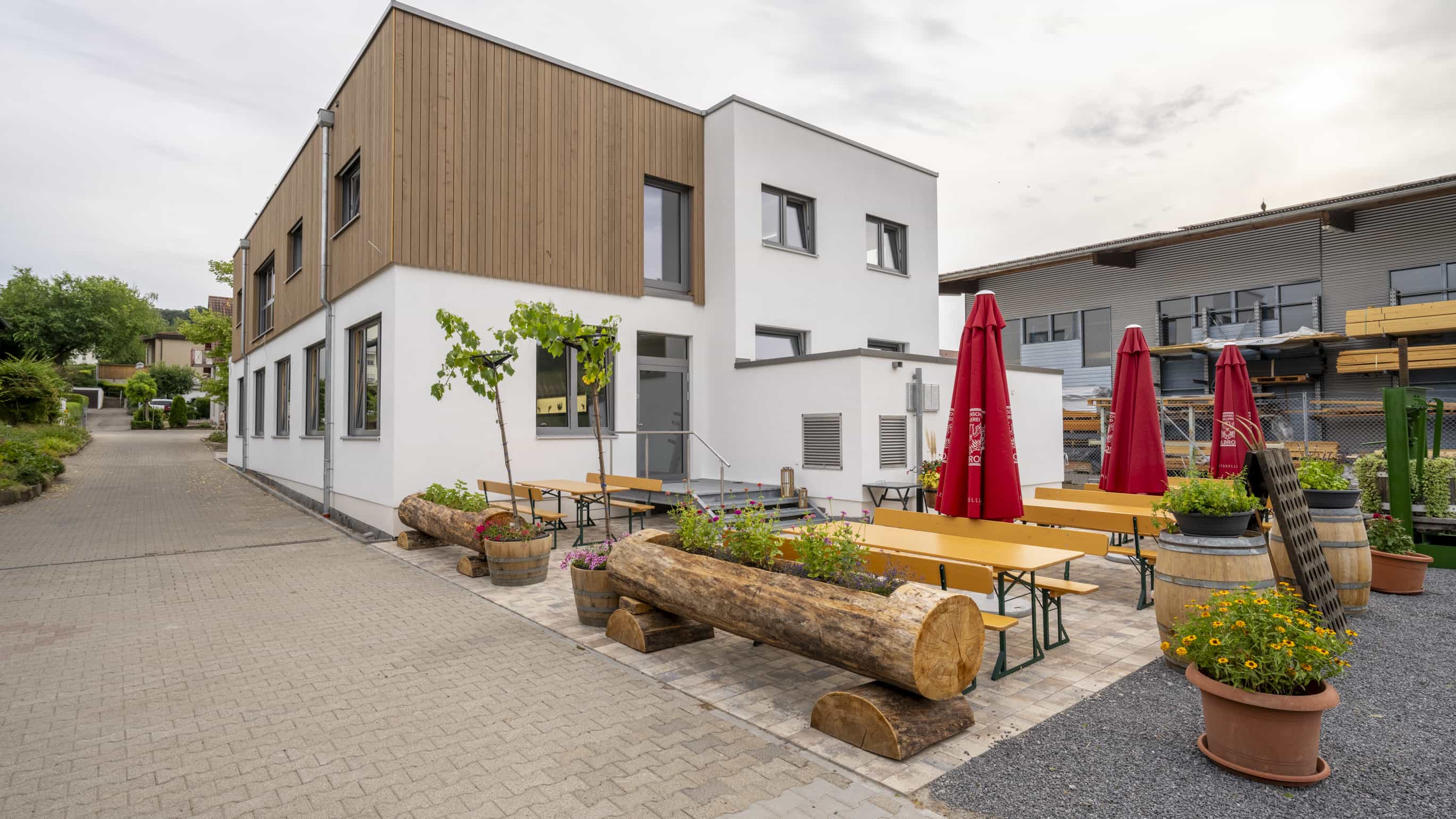 Außenansicht der Weinwirtschaft Burgblick mit Biergarten, Holzbänken und roten Sonnenschirmen vor dem Gebäude
