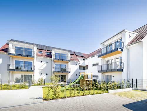 Weiße Mehrfamilienhäuser mit Balkonen und Spielplatz, Haas Wohnbauprojekt Eching zum Ratgeber Einliegerwohnung Mietrecht