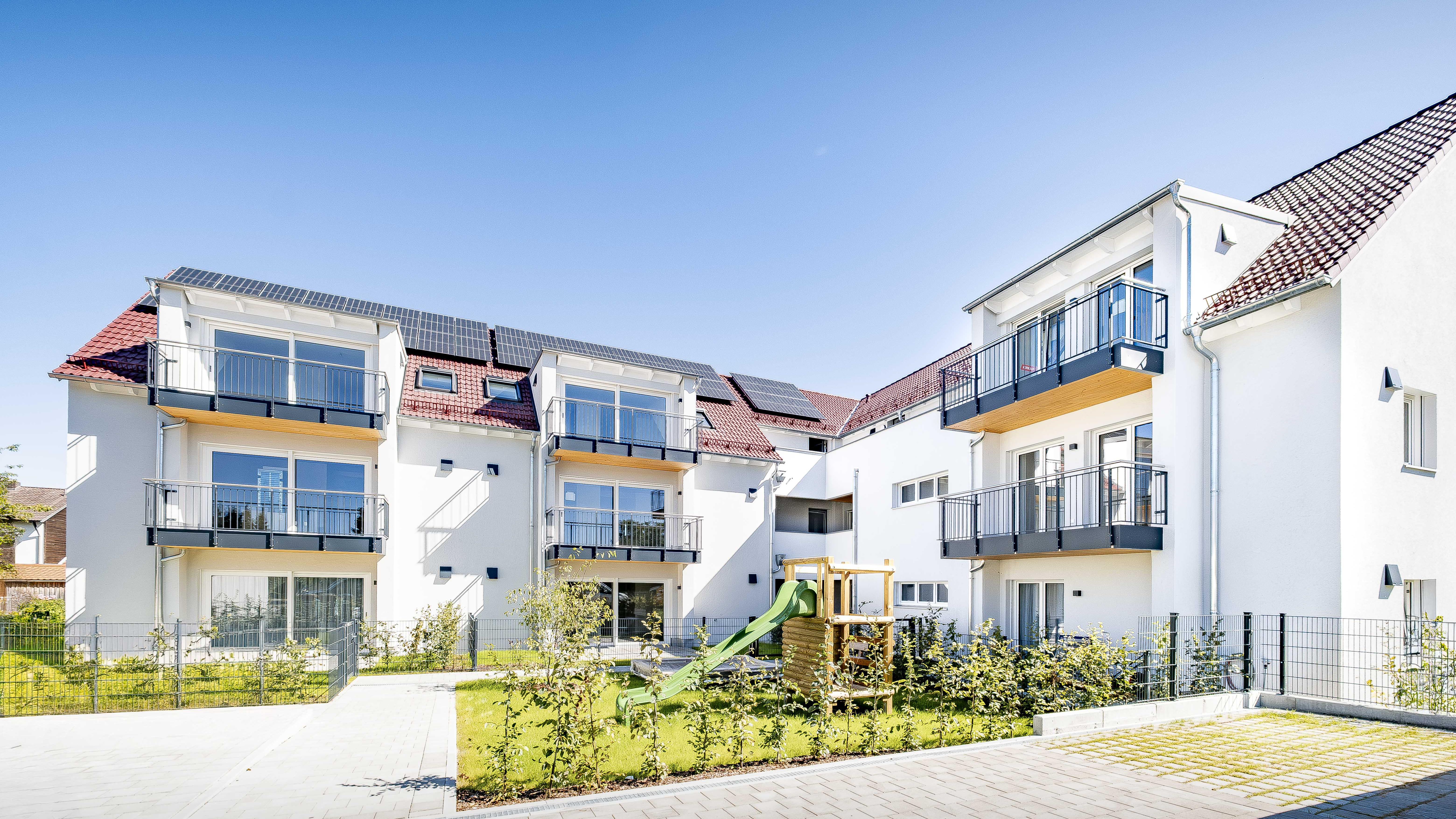 Weiße Mehrfamilienhäuser mit Balkonen und Spielplatz, Haas Wohnbauprojekt Eching zum Ratgeber Einliegerwohnung Mietrecht