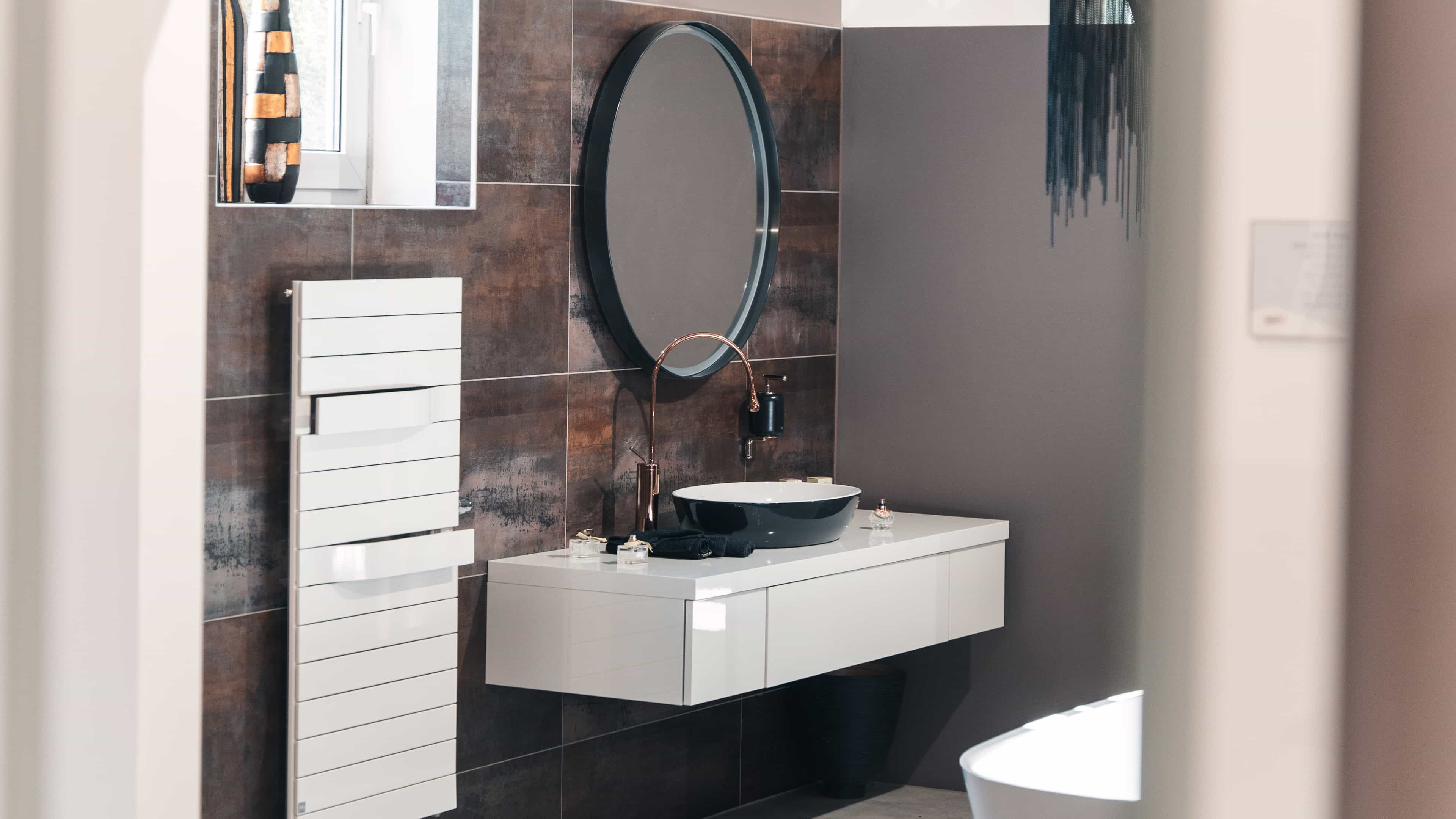 Modernes Badezimmer mit rundem Spiegel, schwarzem Waschbecken, Kupferarmatur und weißem, wandmontiertem Waschtisch.