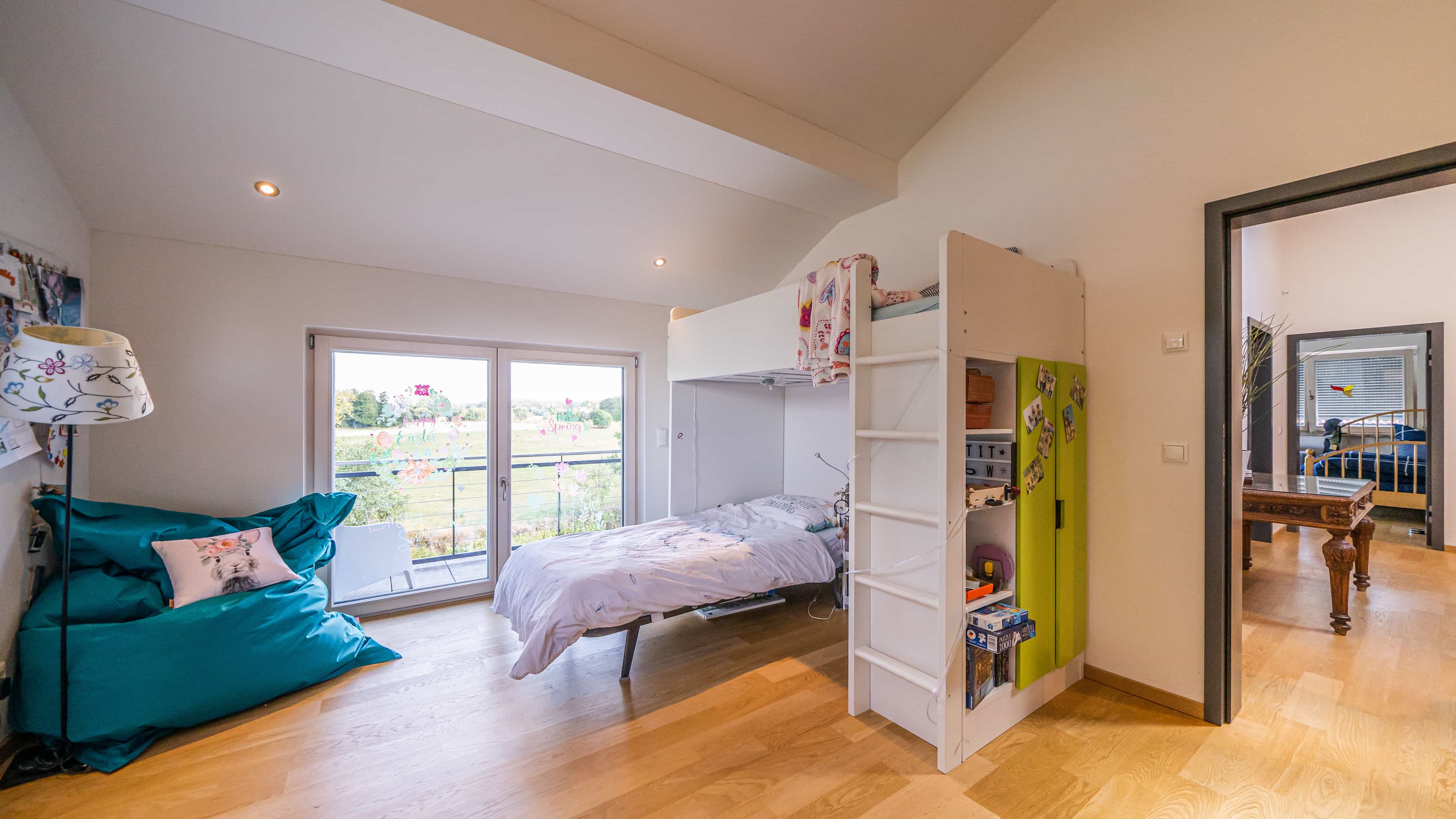 Kinderzimmer mit Hochbett, blauem Sitzsack und Balkontür im wohngesunden Haas Fertighaus