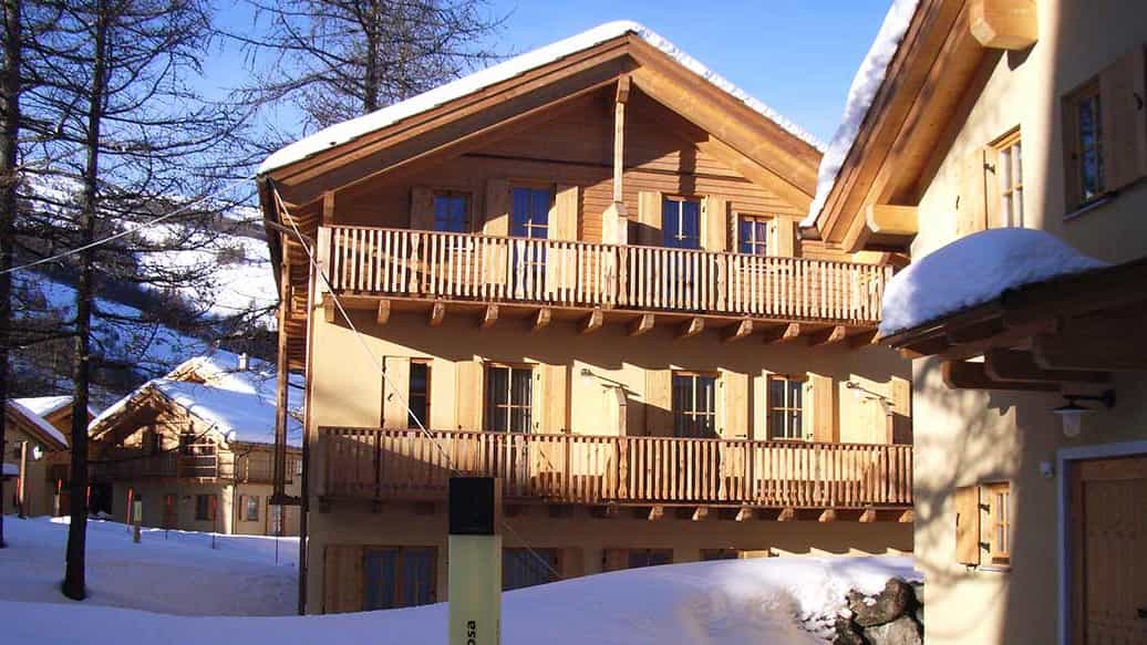 Chalet im Holzbau mit umlaufenden Holzbalkonen im Schnee in der Ferienwohnanlage Pragelato von Haas Fertigbau