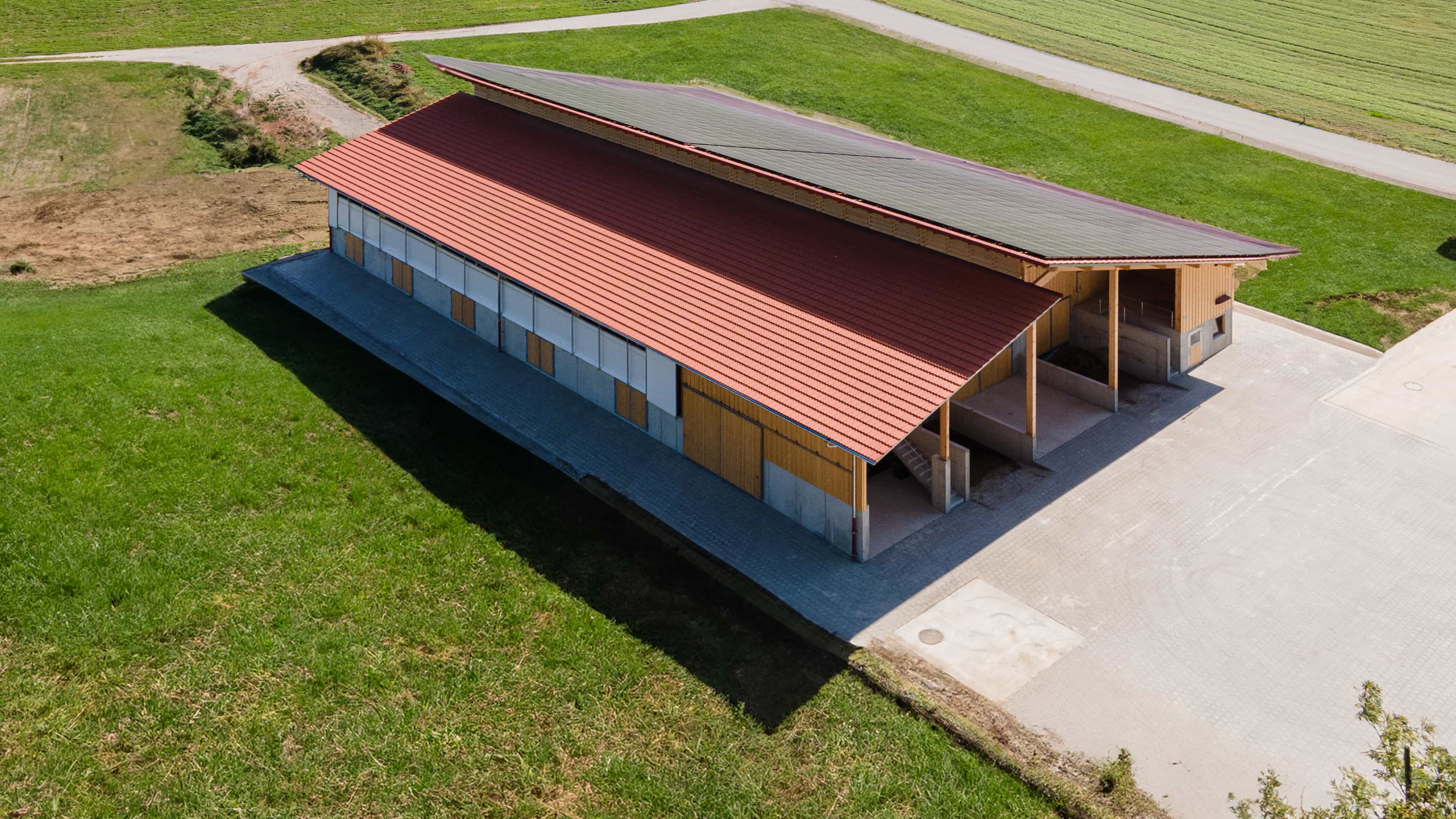 Luftaufnahme des Rinderstalls mit rotem Dach und Photovoltaik am Feldrand