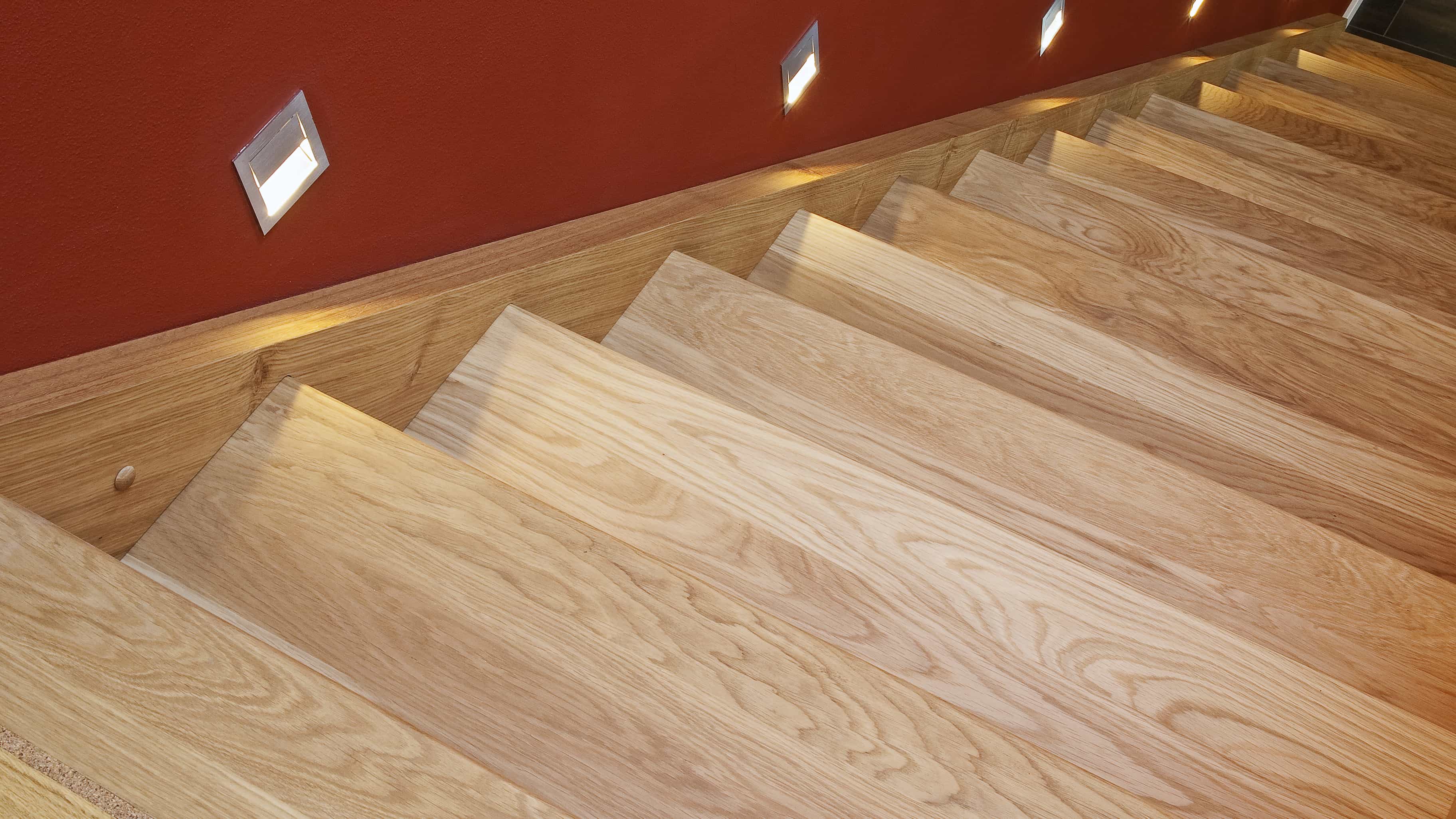 Detail der Holztreppe mit roter Wand und Beleuchtung im Musterhaus Haas MH Poing 187