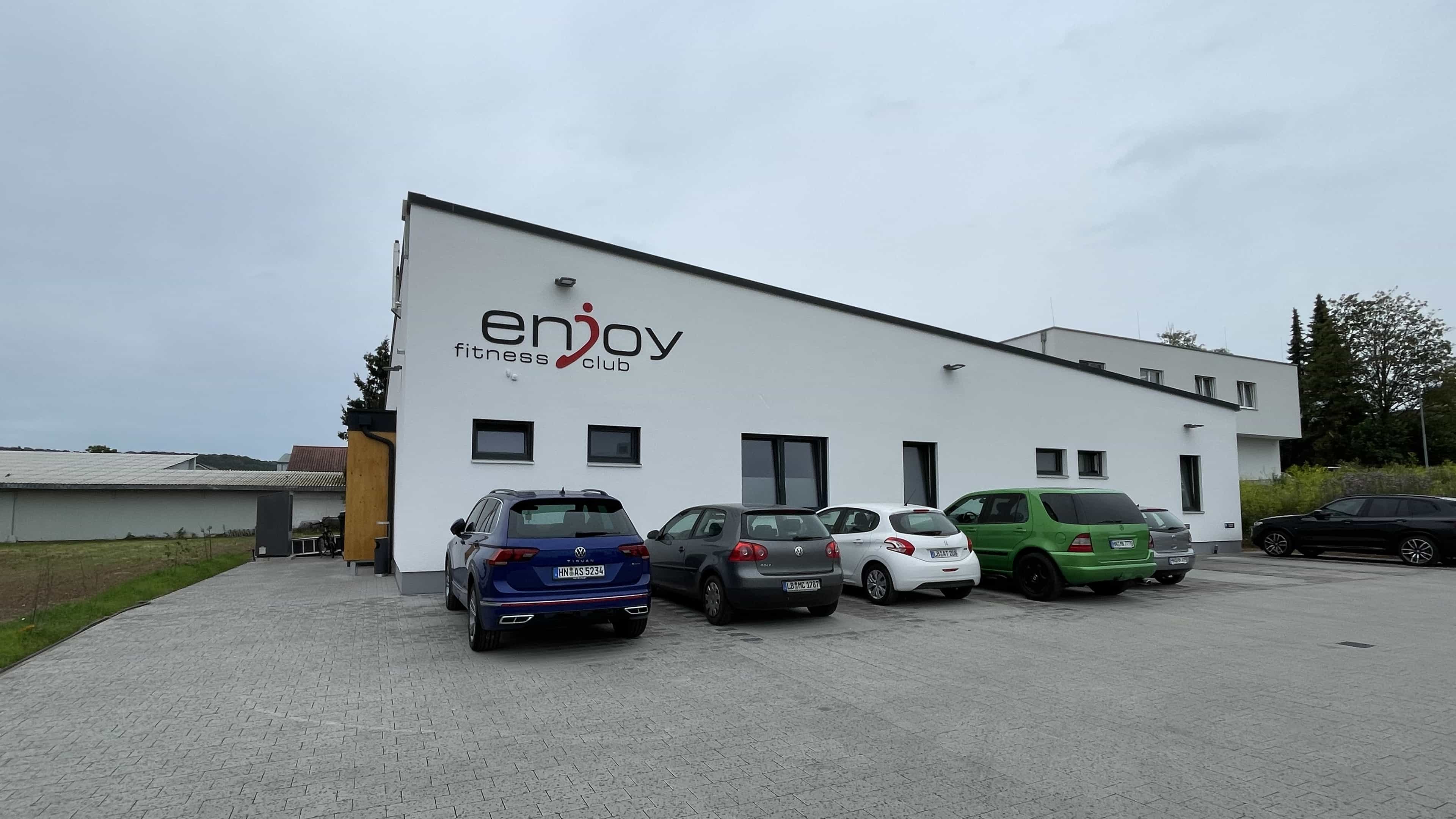 Neubau des Fitnesscenters Enjoy Fitness mit weißer Fassade, Logo und Parkplatz von Haas Gewerbebau