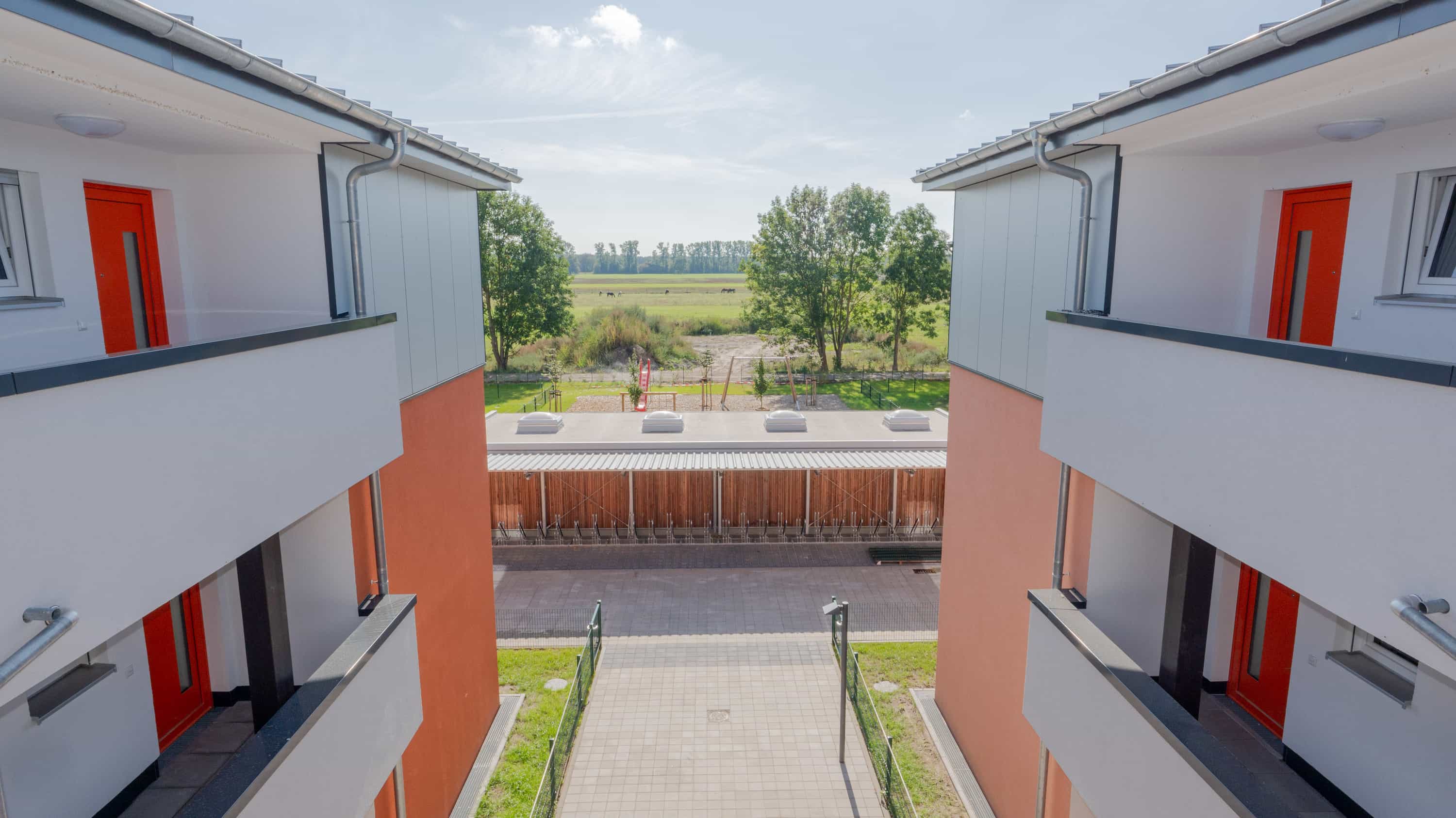 Blick zwischen zwei Mehrfamilienhäusern mit Laubengängen und roten Türen im Quartier Zum Glück Bötzow