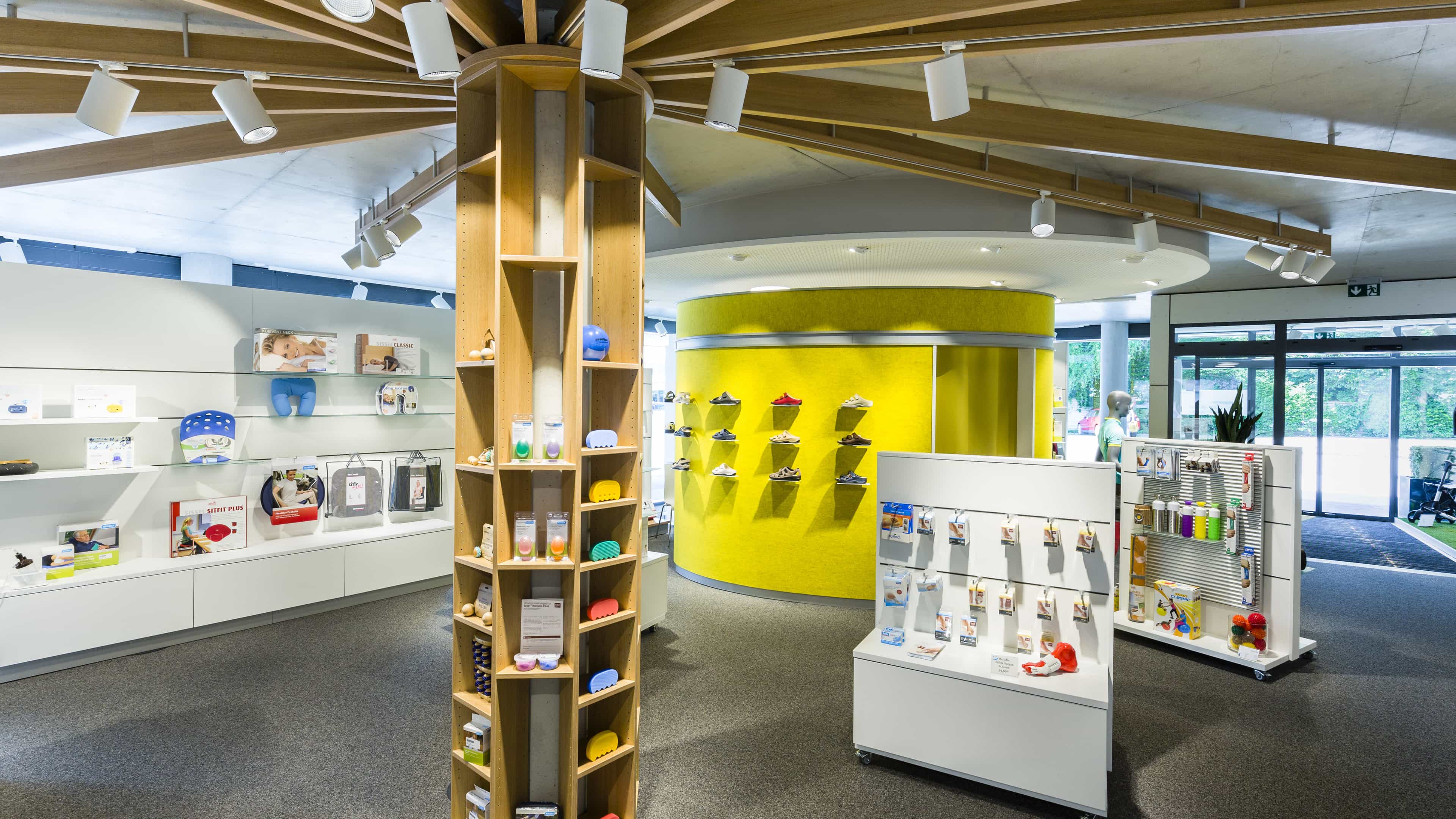 Ausstellungsraum mit Holzsäule, gelber Rundwand und Produktdisplays, Haas Ausstellungs- und Verkaufsgebäude