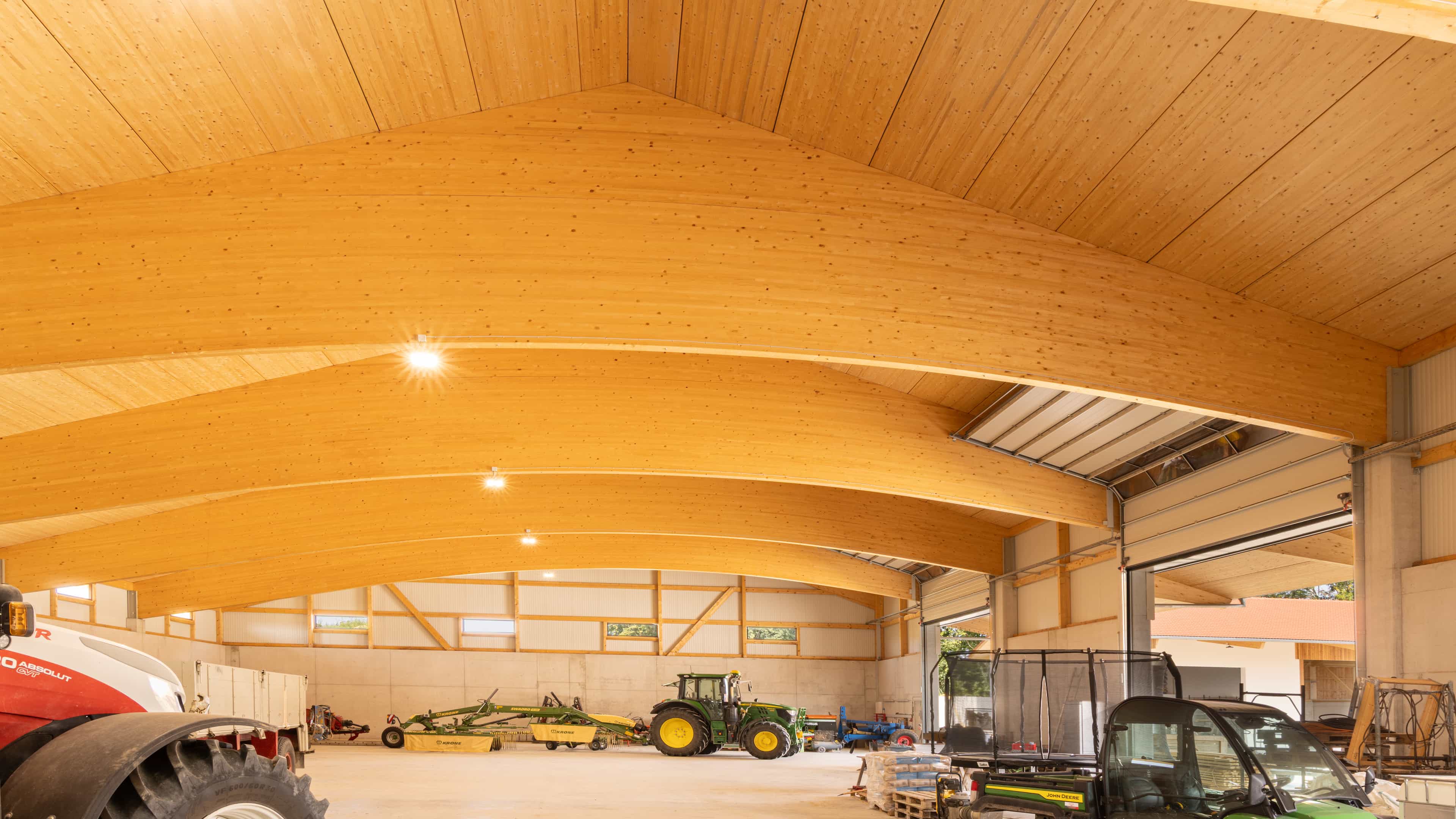 Große landwirtschaftliche Maschinenhalle mit Holzbalkendecke und mehreren Traktoren im Inneren.