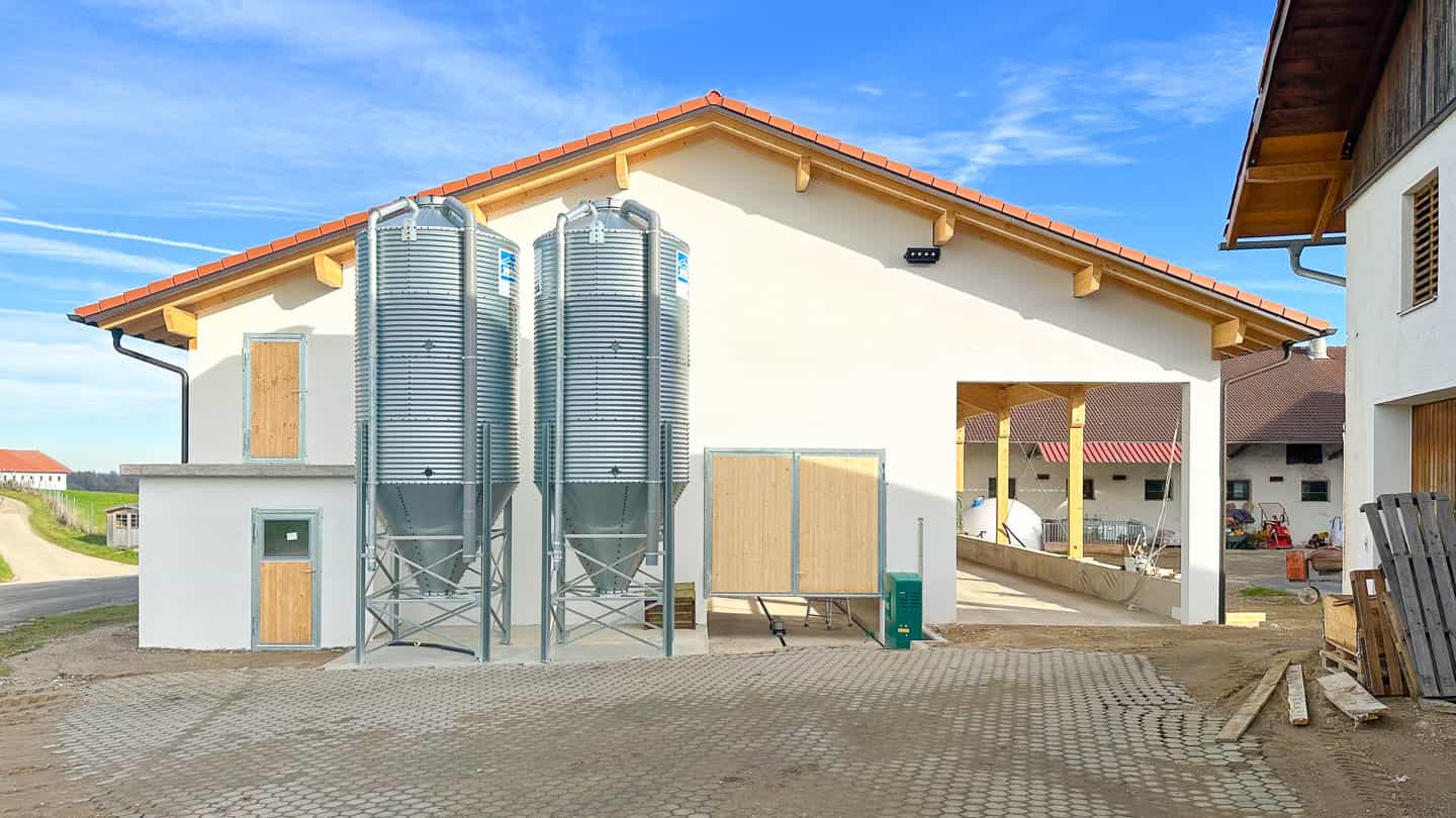 Rindermaststall in Polling mit zwei Futtersilos, weißer Fassade und Holzgiebel