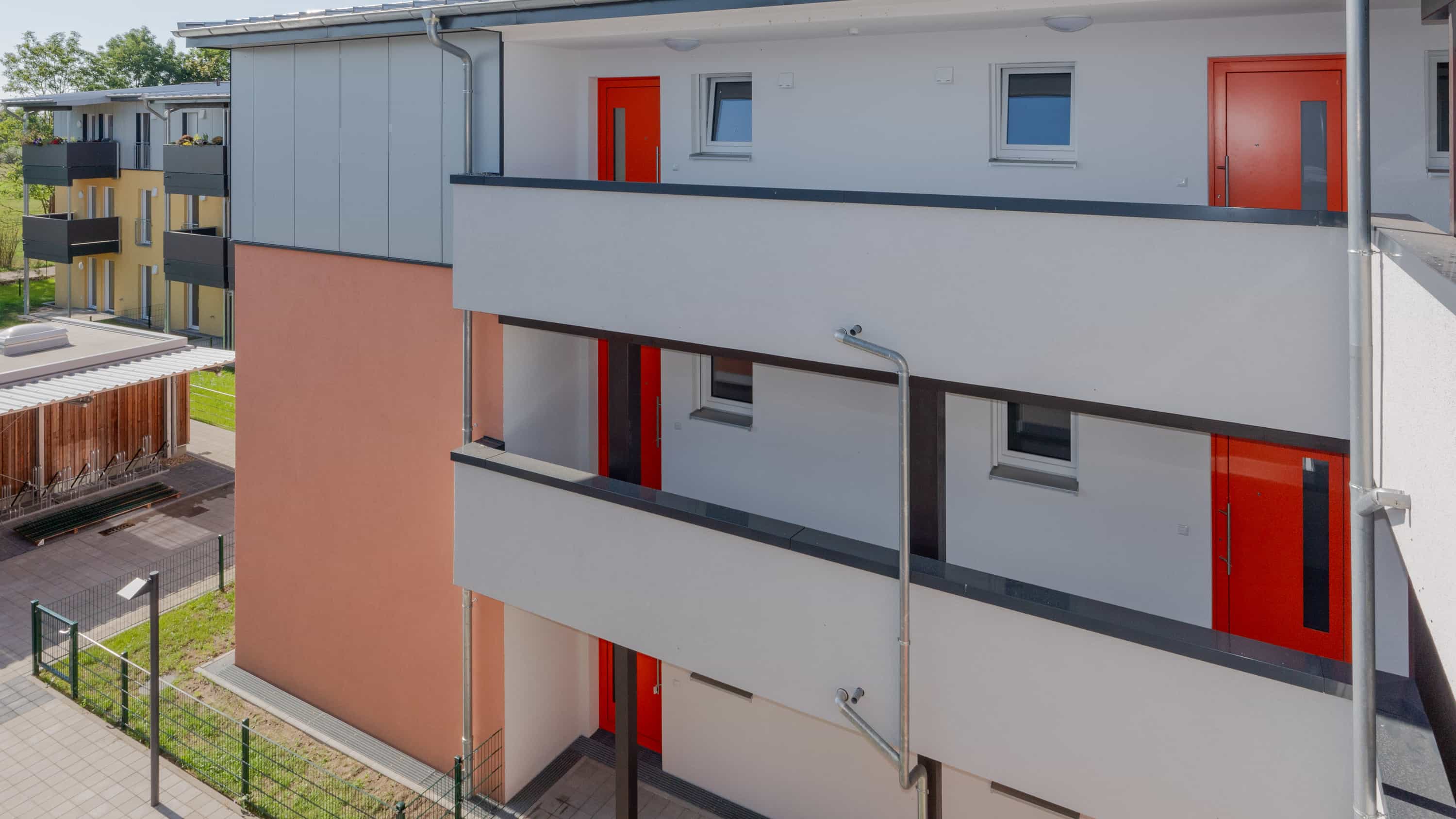 Laubengänge mit roten Wohnungstüren und orangefarbenem Fassadenfeld an einem Mehrfamilienhaus in Bötzow