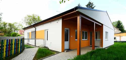 Kindergarten Roztoky von Haas Fertigbau mit weißer Fassade, orangen Akzenten und überdachtem Eingang