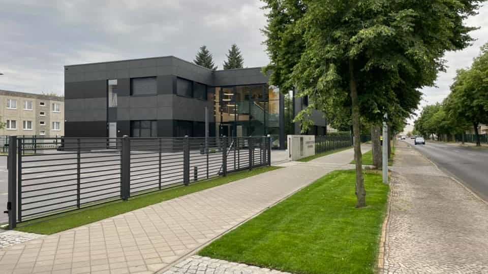 Straßenansicht des Gesundheitszentrums Steidten Oranienburg mit Zaun, Rasenstreifen und Bäumen