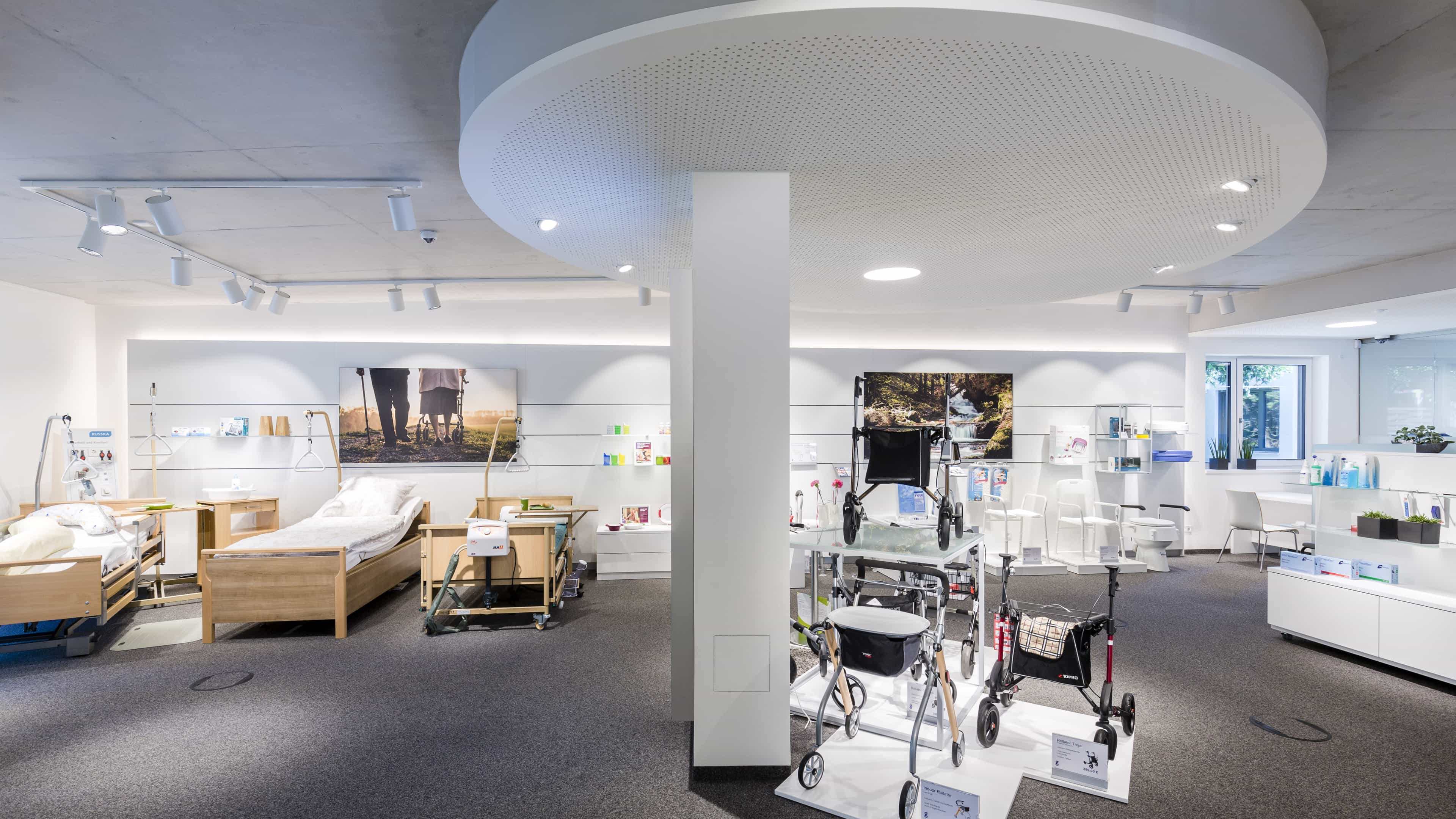 Verkaufsraum eines Sanitätshauses mit Pflegebetten und Rollatoren unter runder Lichtdecke, Haas Verkaufsgebäude
