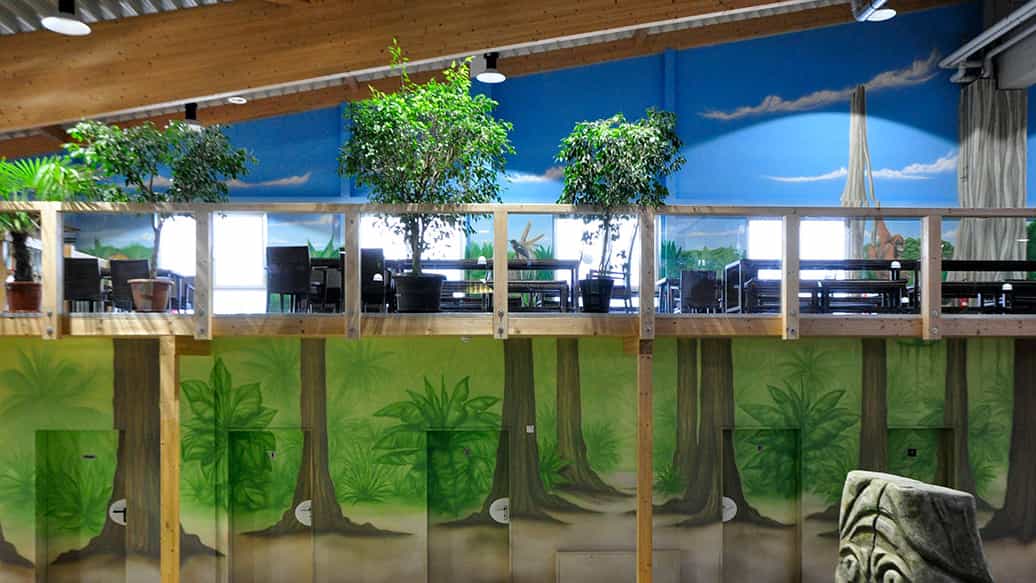Wandmalerei mit Dschungelbäumen vor dem Sitzbereich im Kibungu Indoor-Spielparadies