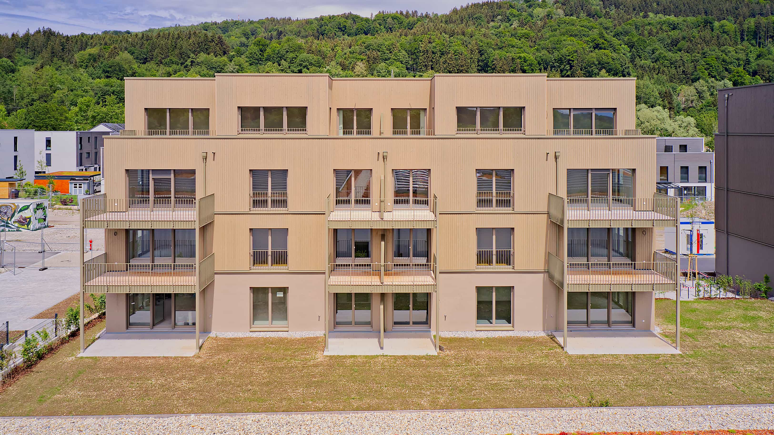 Frontansicht eines der drei Mehrfamilienhäuser mit insgesamt 35 Wohnungen im Pfaffenwinkel vor dem Waldhang