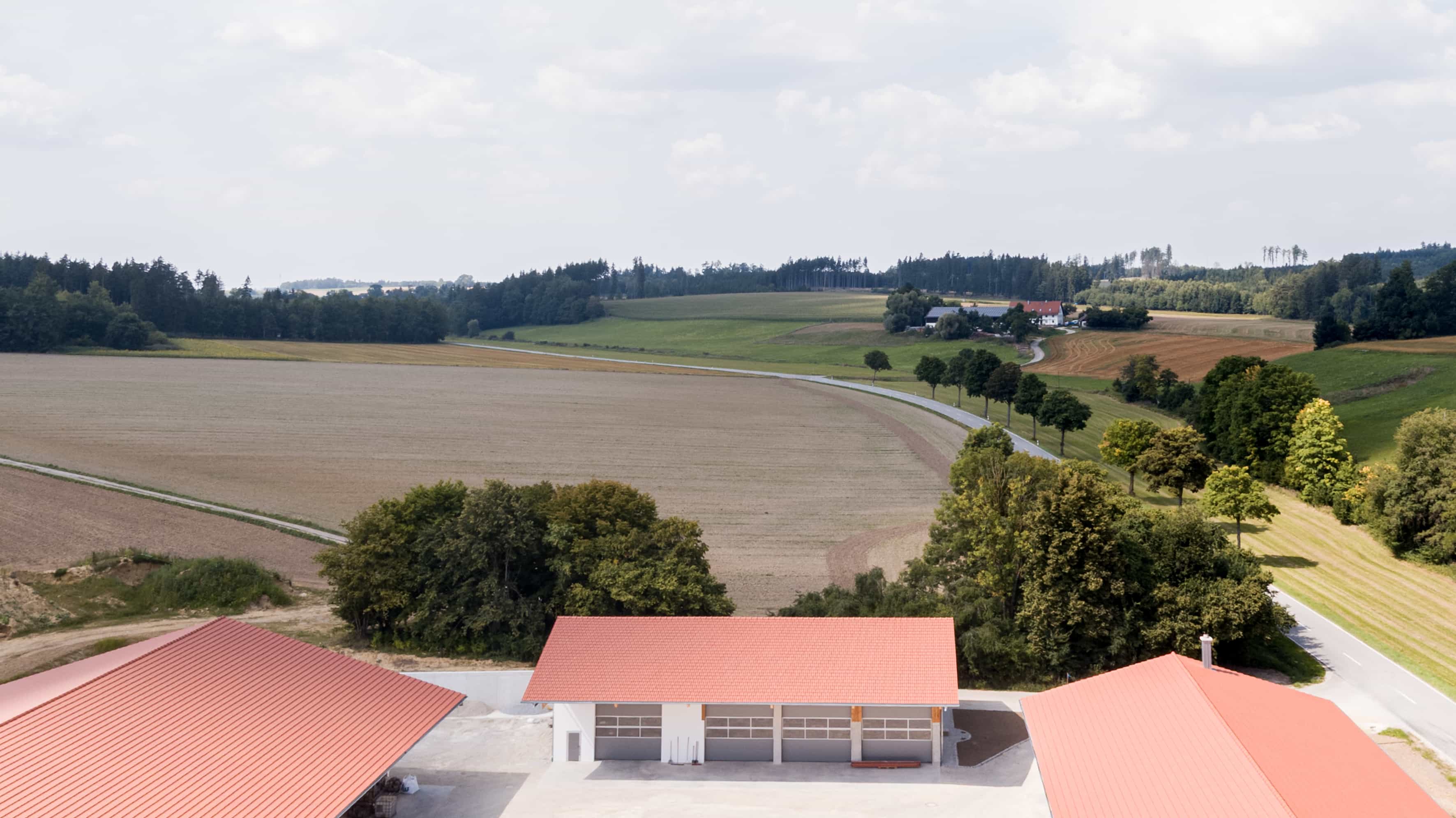 Luftbild eines landwirtschaftlichen Gebäudekomplexes mit roten Dächern, umgeben von Feldern und Bäumen im ländlichen Umland.