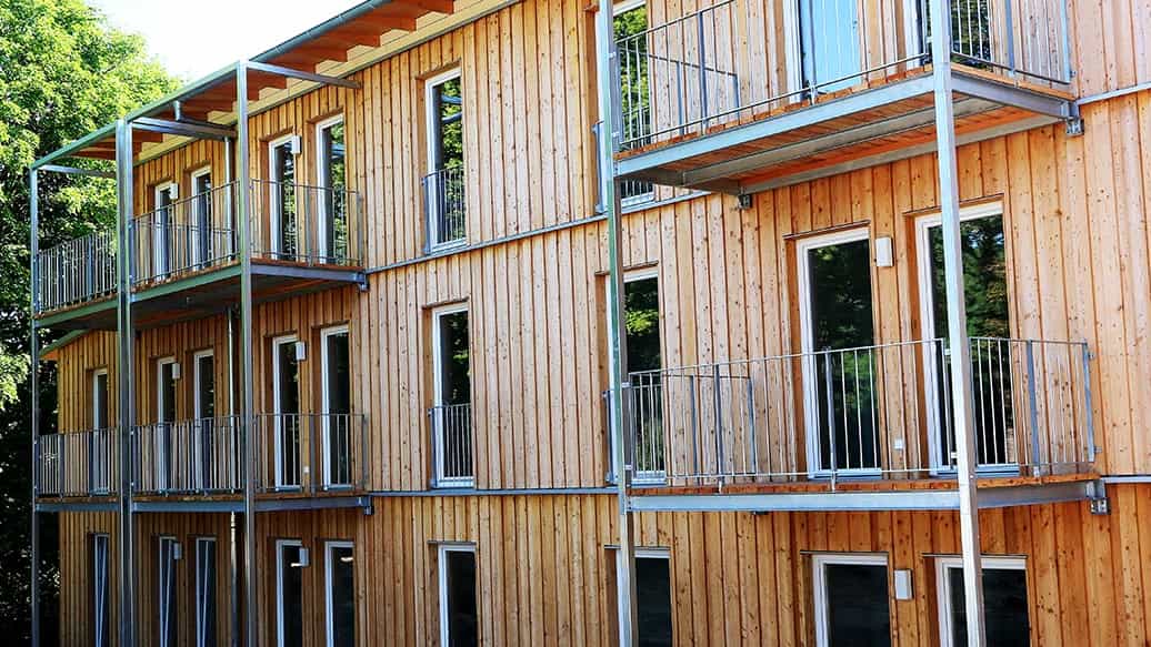 Balkone mit Stahlgeländern an der Holzfassade des dreigeschossigen Sozialwohnungsbaus von Haas Fertigbau